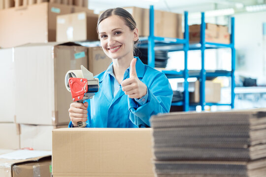 Woman in factory warehouse packaging goods giving thumbs-up
