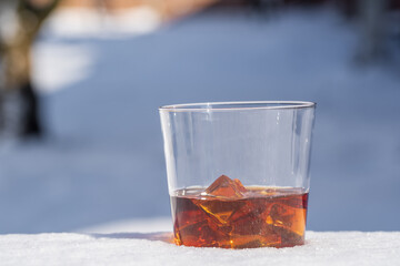 Glass of whiskey with ice on a bed of snow and white background, close up