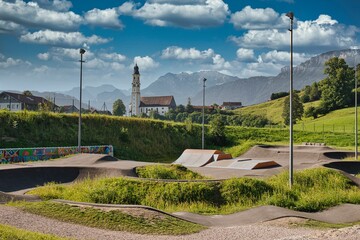 a modern pumptrack / skatepark with a catholic church in and mountains in the background