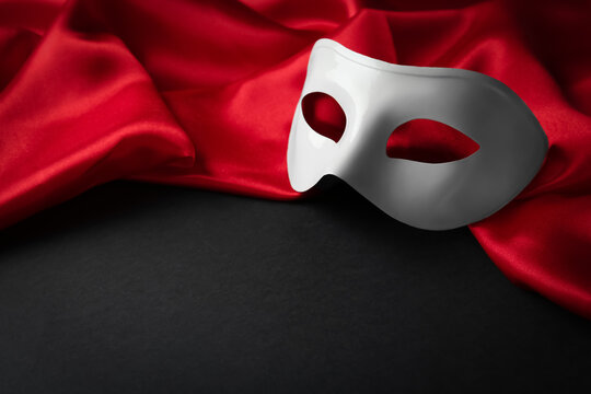 White theatre mask and red fabric on black background. Space for text