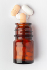 Macro Close up of medicinal or herbal tablet spilled and in an amber glass bottle. Top view, white background.