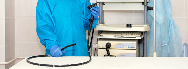 Doctor gastroenterologist in protective clothing holding endoscope before gastroscopy. Medical examination, medicine utensils and instruments, gastrointestinal fiberoptic endoscopy at modern hospital.