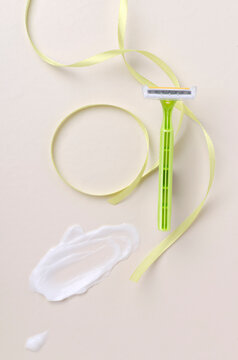 Vertical image of razor, decorative ribbon and whit cream for depilation