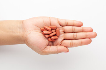 Macro Close up of medicinal or herbal dark brown tablet on female hand palm. Top view, white background.