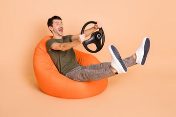 Full size photo of young handsome crazy smiling sit armchair riding fast hold steering wheel...