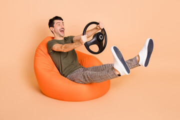 Full size photo of young handsome crazy smiling sit armchair riding fast hold steering wheel isolated on pastel color background