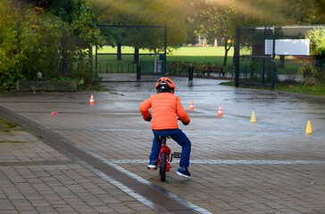 Rear view School kid learns to ride a bike in the Park, Outdoor Portrait of a young boy practicing how to ride a bicycle  , Child in helmet riding a cycling in the morning.