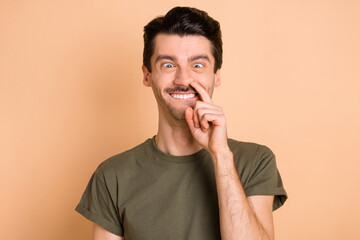 Photo portrait of guy put finger in nose silly idiot comedian isolated on pastel beige color background