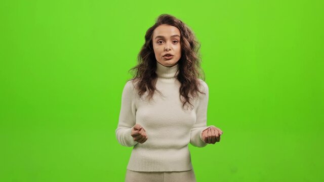 The woman is standing and looking at the camera. She is waving her hands and talking. She is standing on a green background. Green screen. 4K