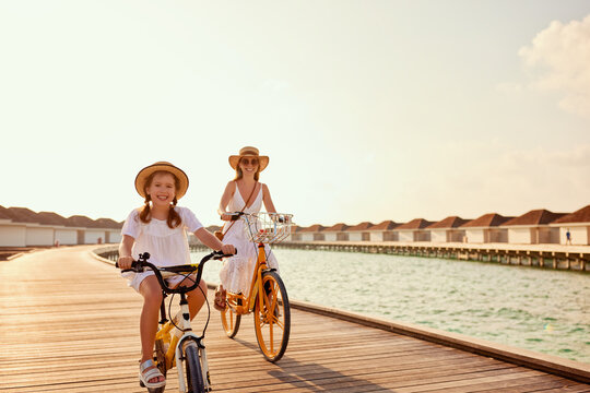 Carefree mother and daughter riding bicycles along wooden promenade
