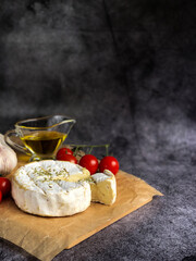 Brie cheese on a black background with vegetables with copy space
