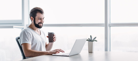 Website header of Portrait of smiling man sitting in the office with laptop and coffee. Side view