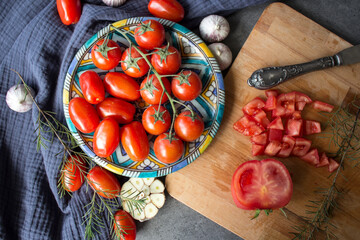 Chopped tomatoes, garlic bulbs, herbs and cherry tomatoes on blue ceramic plate. Food preparation...