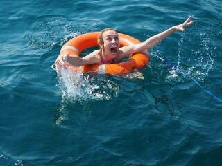 Scared screaming drowning girl in orange lifebuoy in the open blue sea