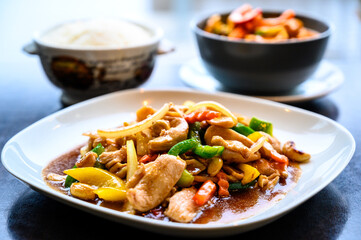 Thai food with chicken, cashew and vegetables on a white plate with a bowl of rice on a side