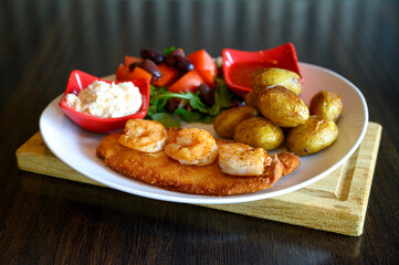 Fried fish topped with tiger shrimp served with baked potatoes and salad and sauce