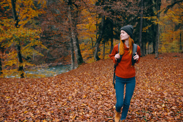 Traveler with a backpack in the autumn forest and hat sweater jeans fallen leaves lake trees