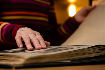 Elderly woman looks through an family album with old photos at table at home. Granny memories past times and remembering his life.