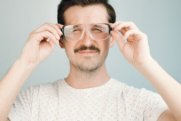 Young man in big glasses squints at the camera, close-up. Health problem concept, low vision,...