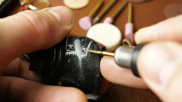 A professional engraver creates a piece of jewelry by making grooves with a special cutter.