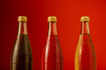 Three fresh chilled lemonade bottles with red, yellow and green liquid on the background and with...