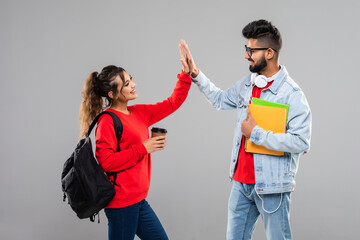 Two happy smiling indian students standing with backpacks and giving high five isolated on the gray...