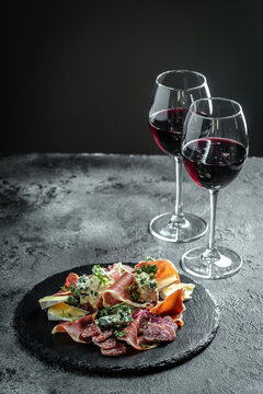 Antipasto platter. Glass of red wine with various cheeses and prosciutto on a black background. vertical image, place for text