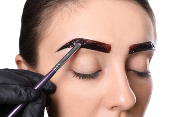 Beautician applying tint during eyebrows correction procedure on white background, closeup