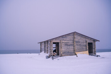 The wooden house in winter has a lonely atmosphere. The location is on the coast of the Barents Sea in Russia.