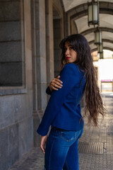 Fototapeta premium Young woman posing for a portrait holding her shoulder. She wears jeans and an blue American jacket. The photo was taken in La Laguna, Tenerife.