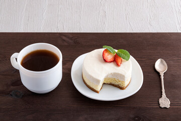 Cheesecake, teaspoon and cup of coffee on dark wooden background. Dessert in cafe.