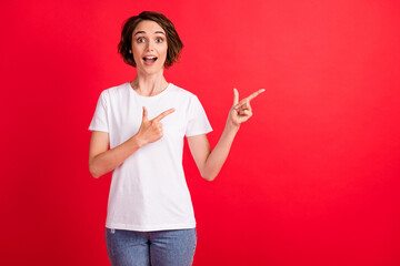 Portrait of attractive amazed cheerful girl demonstrating new offer ad novelty isolated over bright red color background