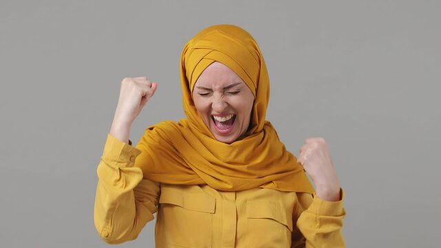 Fun arabian asian muslim woman in abaya hijab yellow clothes countdown 1 2 3 one two three go celebrate win scream rejoices doing winner hands gesture clenching fist isolated on grey gray background