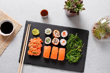 Sushi takeaway with sushi set, wakame salad, chopsticks and sauces on gray concrete background, top view