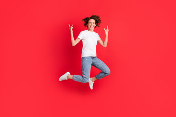 Full length body size view of attractive crazy overjoyed cheerful girl jumping showing horn symbol isolated over bright red color background