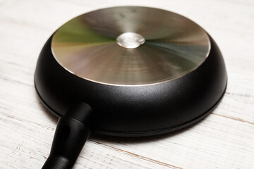 Bottom, back side of a new aluminum frying pan on a white wooden background.