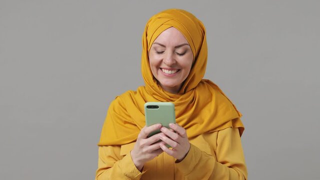 Dreamful young arabian asian muslim woman in abaya hijab yellow clothes hold use mobile cell phone typing browsing chatting send sms isolated on grey gray background People uae islam religious concept