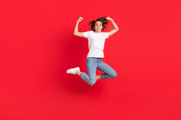 Full length body size view of attractive funny girl jumping demonstrating muscles fooling isolated over bright red color background