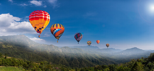Colorful hot air balloons flying above green nature mountain with blue sky background.