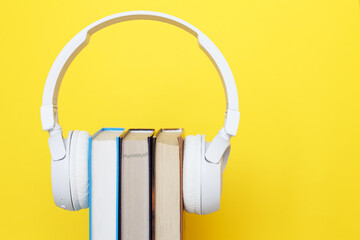 Audio book concept with modern white headphones and hardcover book on a yellow background. Listening to a book.