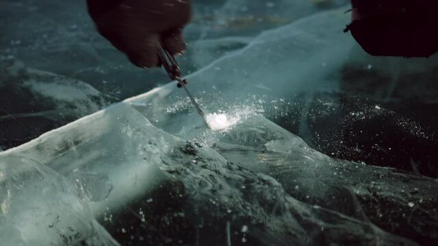 Close-up. Man's hands pierce a hole in the ice with a knife to pour wine for those who perform the traditional local ritual "Kiss with Baikal".