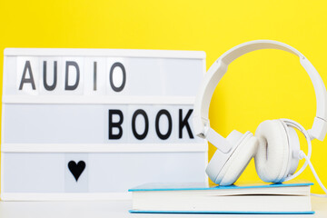 Audio book concept with modern white headphones and hardcover book on a yellow background....