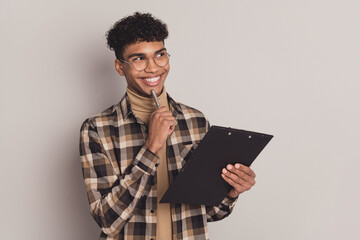 Photo portrait of dreamy curious guy writing exam on clipboard interview looking blank space smiling isolated on grey color background