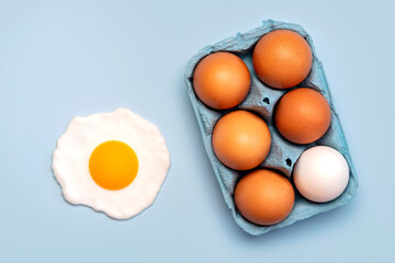 Top view of chicken eggs in an open blue cardboard box and a fried egg