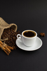 Black coffee in the white cup,cinnamon and coffee beans on the black background. Location vertical.