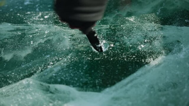 Close-up. Man's hands pierce a hole in the ice with a knife to pour wine for those who perform the traditional local ritual "Kiss with Baikal".