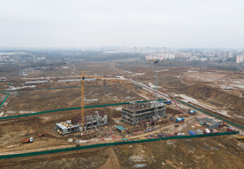 Drone view of a large construction site. Tower cranes in action on fog background. Housing renovation concept. Crane during formworks. Construction the buildings and multi-storey residential homes