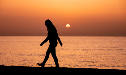 Fototapeta na wymiar Silhouette of a woman walking by the ocean. Woman shilouette at sunrise on the beach