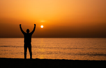 Silhouette of a man by the ocean. Man shilouette at sunrise on the beach.  Man with victory expression
