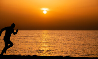 Silhouette of a man running by the ocean. Man shilouette at sunrise on the beach